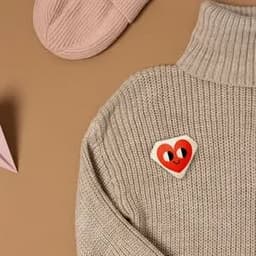 A beige sweater featuring a heart-shaped custom button with a happy face in red and black.