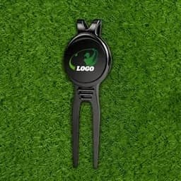 A black divot tool with a circular ball marker featuring a logo, set against green grass.