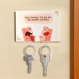 Acrylic keychain featuring two seated figures, with two silver keys attached, on a light background with illustrations.