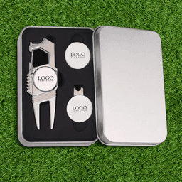 A silver gift box containing a divot tool and two ball markers, all with a logo, set against artificial grass.