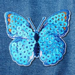 A blue sequin butterfly patch with varying tones of blue and sequins, stitched onto a denim background.