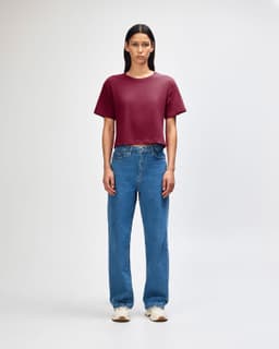 A woman stands wearing a burgundy boxy T-shirt and light blue cargo jeans, paired with black and white sneakers.