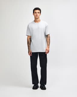 A heavyweight cotton unisex T-shirt in light grey, worn by a person with olive green trousers and sneakers.