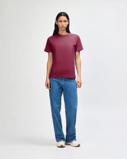 A unisex heavyweight cotton t-shirt in maroon, worn with light blue baggy jeans and black sneakers, featuring a logo.