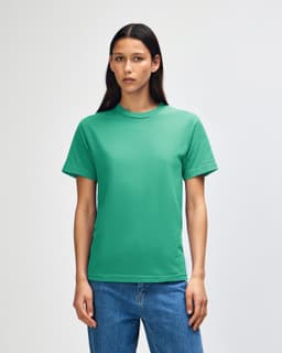 A green heavyweight cotton unisex T-shirt displayed on a model with curly hair, set against a plain background.