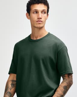 A heavyweight cotton unisex t-shirt in dark green, worn by a model with curly hair. Features a simple, classic design.