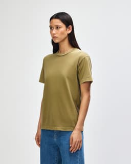 A heavyweight cotton unisex T-shirt in olive green, displayed on a model with curly hair. It features a simple design and branding.
