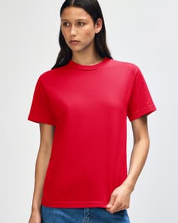 A red heavyweight cotton unisex T-shirt displayed on a model with curly hair. The shirt has a logo on it.
