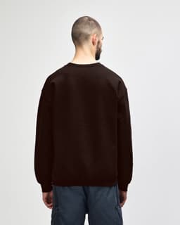 A brown Gildan Heavy Blend adult crewneck sweatshirt, viewed from the back, paired with blue jeans.