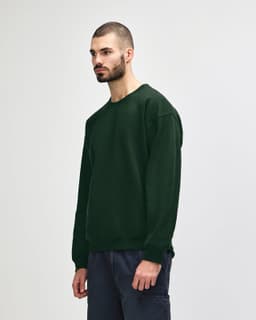 A model wearing a dark green Gildan Heavy Blend Adult Crewneck Sweatshirt, featuring a logo on the sleeve.