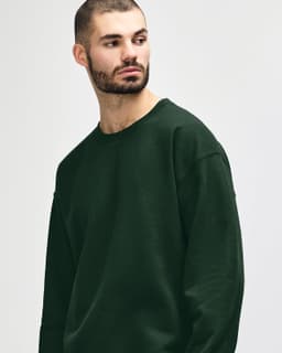 A green crewneck sweatshirt worn by a person, featuring a logo on the sleeve.