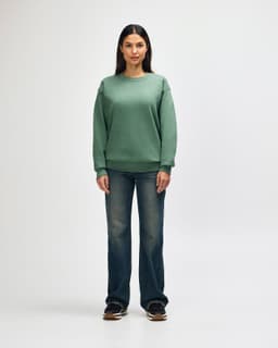 A green Gildan Heavy Blend adult crewneck sweatshirt worn by a model with black jeans and black sneakers. It has a logo.