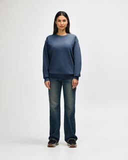 A blue Gildan Heavy Blend crewneck sweatshirt on a model paired with black jeans and sneakers. The sweatshirt has a logo.