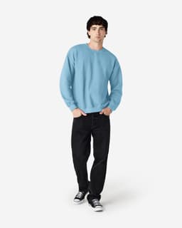 A light blue Gildan Heavy Blend adult crewneck sweatshirt is worn by a model with black jeans and sneakers. 