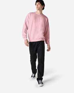 A model wearing a pink Gildan Heavy Blend adult crewneck sweatshirt paired with black jeans and sneakers.
