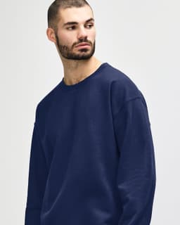 A woman wearing a navy Gildan Heavy Blend Adult Crewneck Sweatshirt, featuring a logo on the front.