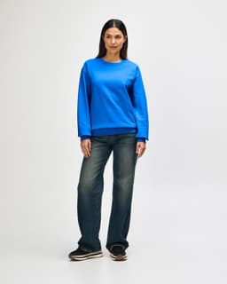 A woman wearing a blue Gildan Heavy Blend crewneck sweatshirt paired with blue jeans and white sneakers.