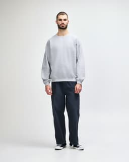 A man wearing a grey crewneck sweatshirt and black jeans, standing in a casual pose against a neutral background.