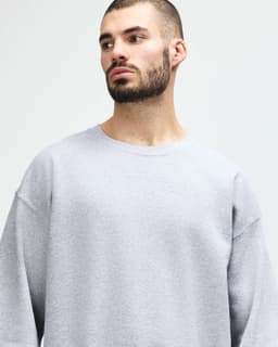 A grey Gildan Heavy Blend adult crewneck sweatshirt displayed on a model posing thoughtfully. It features a logo.