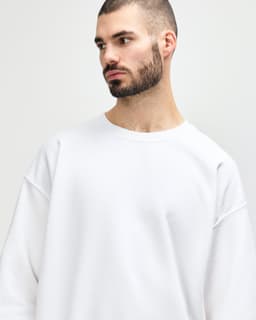 A white Gildan Heavy Blend adult crewneck sweatshirt on a model. The sweatshirt features long sleeves and a relaxed fit.