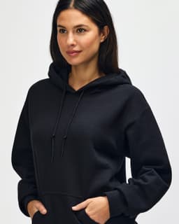 A black Gildan Heavy Blend adult hooded sweatshirt, featuring a drawstring hood and a model adjusting the neckline.