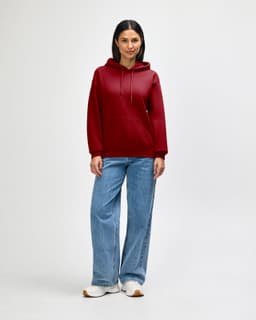 A red hooded sweatshirt with a front pocket, worn by a person in black jeans and sneakers. The sweatshirt features a logo.