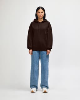 A brown hooded sweatshirt with a front pocket, worn by a model paired with dark jeans and sneakers.