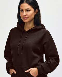 A brown hooded sweatshirt featuring a drawstring hood and a model adjusting it. The design has a logo.