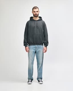 A grey Gildan Heavy Blend adult hooded sweatshirt worn by a model, paired with blue jeans and white shoes.