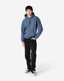 A man wearing a blue hooded sweatshirt and black trousers, standing against a plain background. The sweatshirt has a logo.