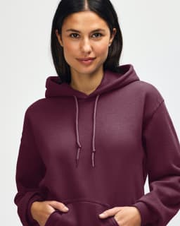 A hooded sweatshirt in a deep burgundy colour, featuring a drawstring hood and an individual adjusting the neckline.