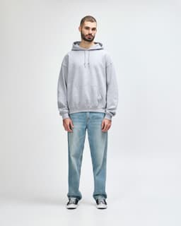 A grey hooded sweatshirt is worn by a male model, paired with black jeans and sneakers. The sweatshirt has a logo.