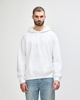 A white hooded sweatshirt with a front pocket and drawstrings, displayed on a model against a plain background.