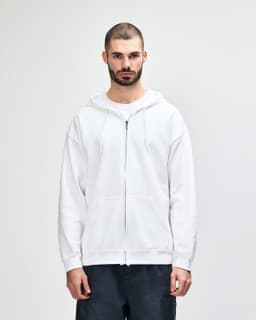 A white full zip hooded sweatshirt on a model, featuring a front pocket and a drawstring hood.