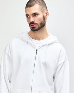 A white Gildan Heavy Blend adult full zip hooded sweatshirt worn by a model adjusting the hood.