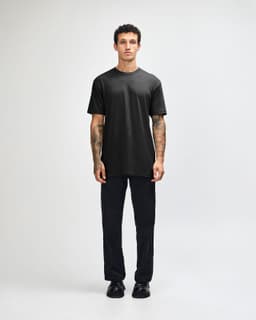 A black unisex short sleeve t-shirt worn with light blue baggy jeans and black sneakers. The model poses against a plain background.