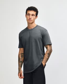 A unisex short sleeve t-shirt in grey, featuring a logo, displayed on a model with tattoos.