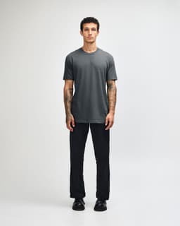 A grey unisex CVC short sleeve t-shirt displayed on a model, paired with black trousers, and featuring a logo.