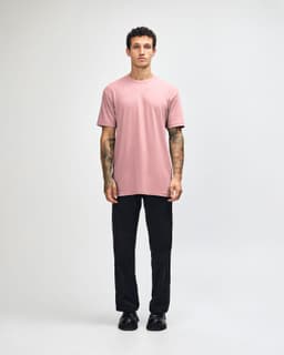 A model wearing a pink unisex CVC short sleeve T-shirt and black cargo pants, featuring a logo.