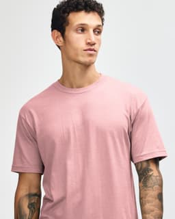 A model wearing a unisex short sleeve t-shirt in a soft pink colour. The shirt features a logo on the sleeve.