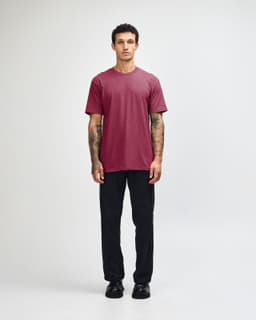 A model wearing a maroon unisex CVC short sleeve t-shirt paired with black trousers and shoes.