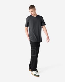 A model is wearing a dark grey unisex CVC short sleeve t-shirt paired with black cargo pants and sneakers.