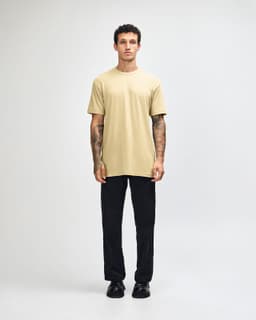 A unisex short sleeve T-shirt in a light khaki colour, worn with black cargo pants, features a logo.
