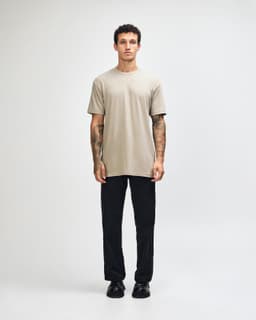 A model wearing an olive green unisex CVC short sleeve t-shirt and black cargo pants, featuring a logo.