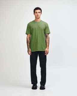 A model wearing a green unisex CVC short sleeve T-shirt paired with black cargo pants and sneakers.