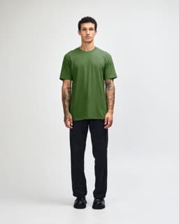 A unisex short sleeve T-shirt in green, worn with black cargo pants. The model is standing with a relaxed pose.