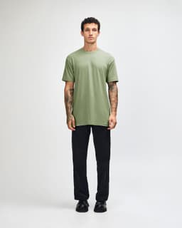A model wearing a green unisex short sleeve T-shirt and black cargo pants, standing in a neutral setting.