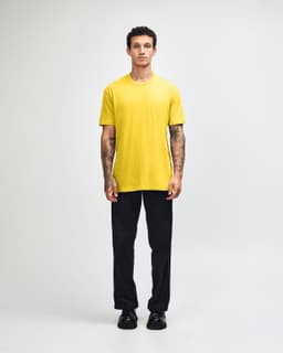 A model wearing a yellow unisex short sleeve T-shirt with black cargo pants and green and white shoes, featuring a logo.