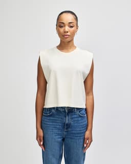 A cream-coloured women's muscle T-shirt with a relaxed, sleeveless design, featuring a logo.