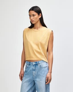 A mustard yellow women's muscle T-shirt with a relaxed fit and short sleeves. The model has curly hair and wears high-waisted jeans.